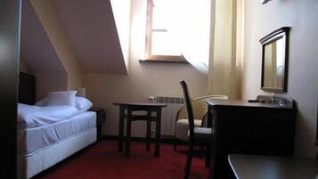 A small, compact room with a bed, a desk, a chair, and a dresser. There is a window providing natural light.