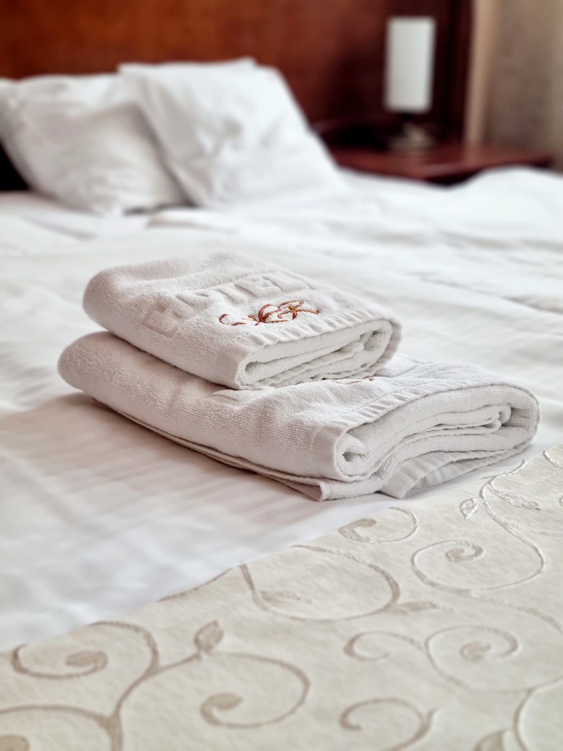 A neatly made bed with folded white towels and a patterned bedspread.