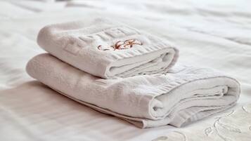 A neatly made bed with folded white towels and a patterned bedspread.