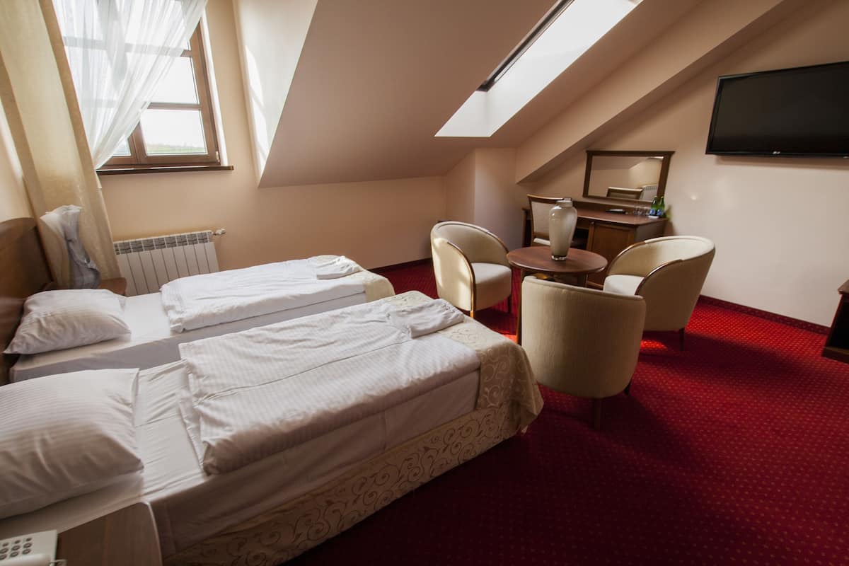 A hotel room with two beds, a desk, a chair, a TV, and a window with curtains.
