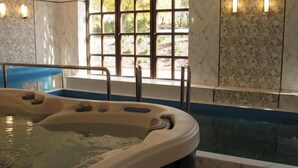 A hot tub with a view of a forest through a window, a blue bench, and a tiled wall with a floral pattern.