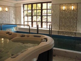 Uma banheira de hidromassagem com vista para uma floresta através de uma janela, um banco azul e uma parede revestida com um padrão floral.