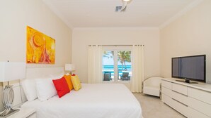 A hotel room with a bed, a TV, a painting, and a view of the ocean.