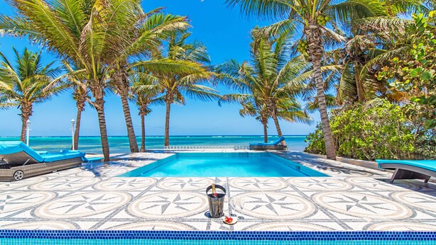 A pool area with a tiled floor, lounge chairs, and a view of the ocean.