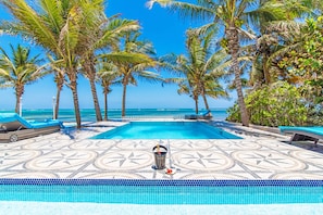 A pool area with a tiled floor, lounge chairs, and a view of the ocean.