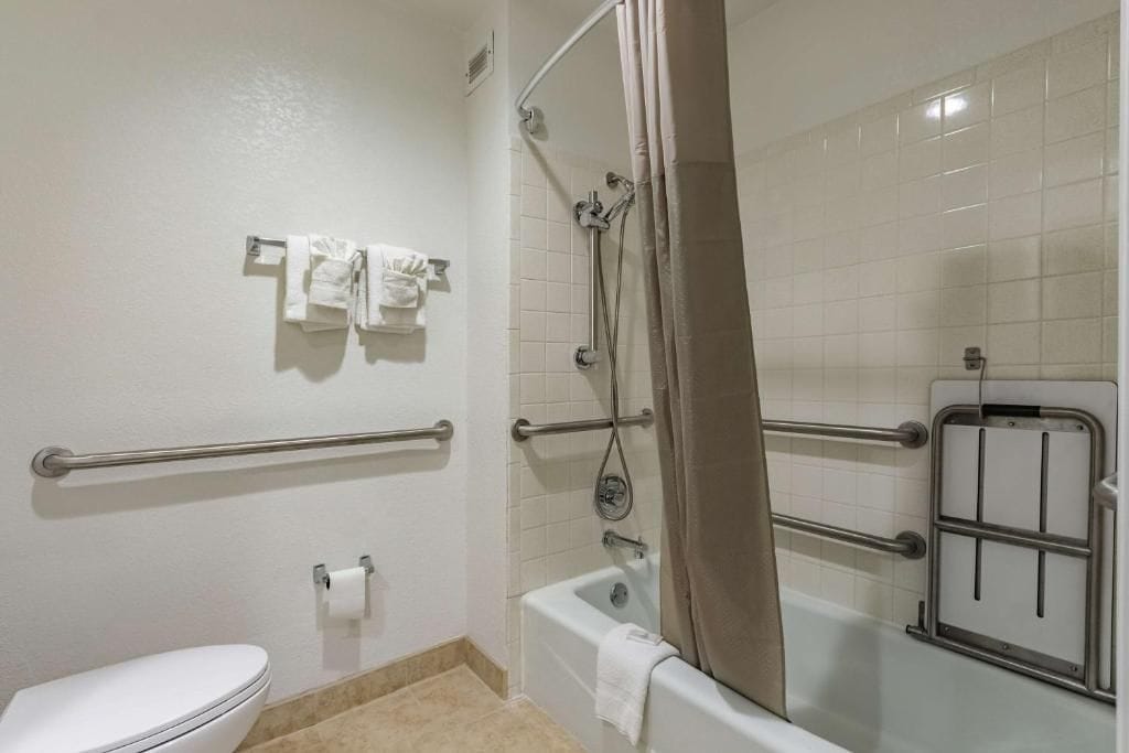 Un bagno con un water bianco, una vasca da bagno con tenda doccia e un mancorrente.