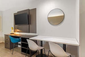 Una habitación moderna con escritorio, dos sillas, televisor y espejo.