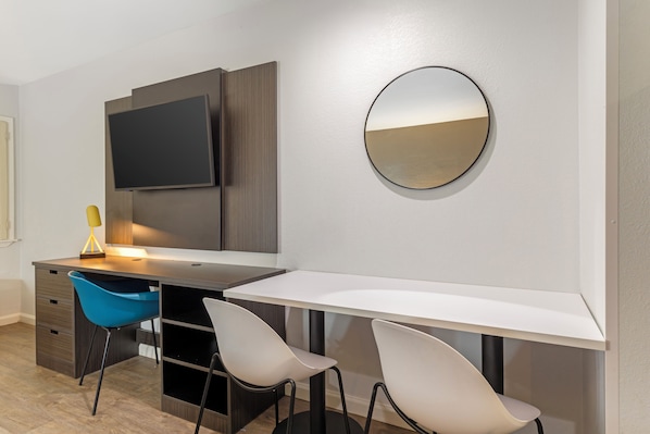 Una habitación moderna con escritorio, dos sillas, televisor y espejo.