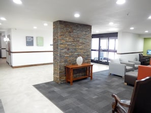 A reception area with a stone pillar, a wooden console table, and a seating area with a grey sofa and an orange chair. - Studio 6 Plano, TX (Plano)