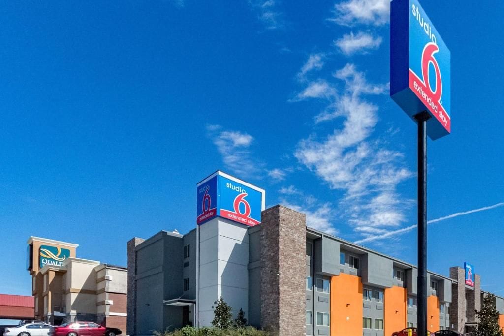 Un hôtel reconnaissable à son grand panneau « Studio 6 Extended Stay », un parking et un ciel d’un bleu éclatant.