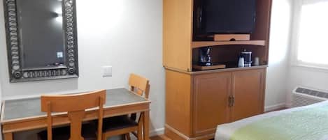 A room with a bed, a wooden desk with two chairs, a television on a wooden cabinet, and a mirror on the wall.