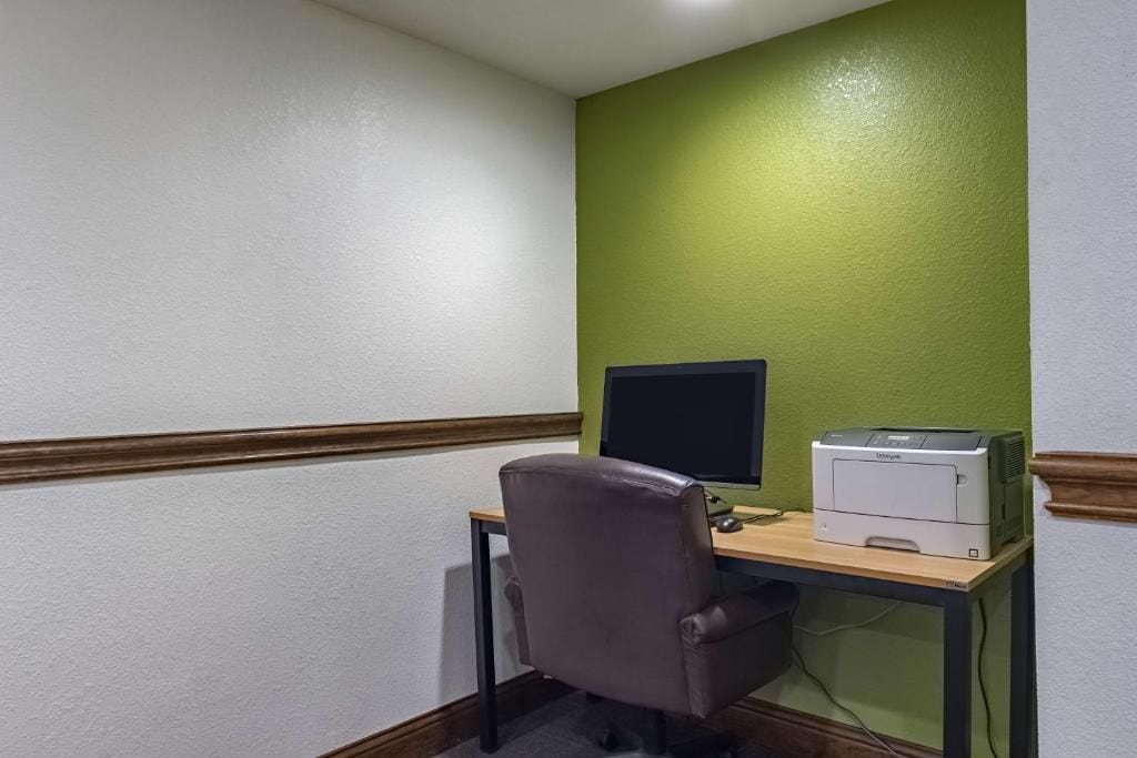 Una oficina en esquina con escritorio, silla, monitor de computadora e impresora.