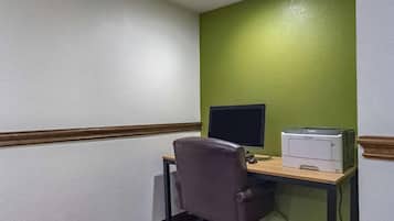 Una oficina en esquina con escritorio, silla, monitor de computadora e impresora.