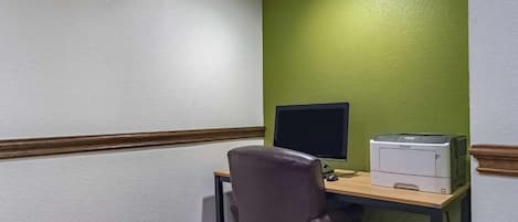 Escritório de canto com mesa, cadeira, monitor de computador e impressora.