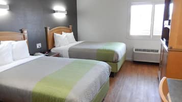 A hotel room with two beds, a wooden floor, a window, and a TV.