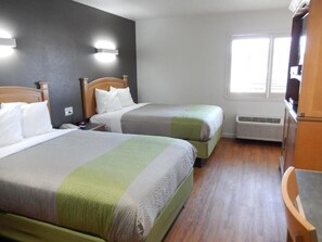 A hotel room with two beds, a wooden floor, a window, and a TV. - Studio 6 Plano, TX (Plano)