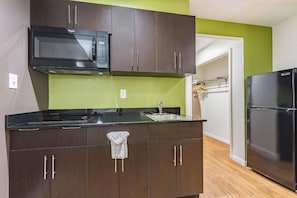 Una cocina con armarios de madera oscura, un microondas negro, un refrigerador de acero inoxidable y una pared de acento verde.