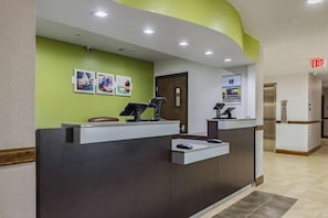 A reception desk with a computer, a telephone, and a chair. There are framed pictures on the wall and an exit sign.