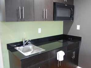 A modern kitchen with dark cabinets, a stainless steel sink, and a black microwave. - Studio 6 Plano, TX (Plano)