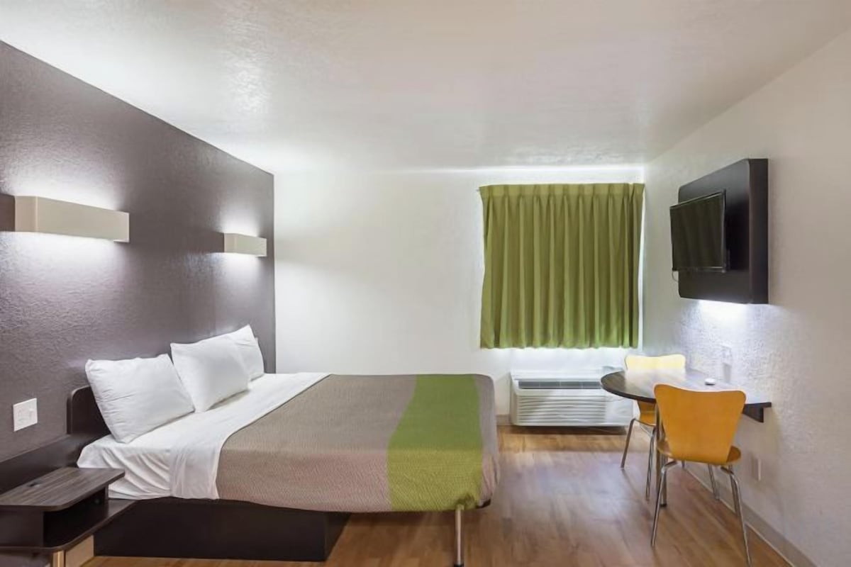 Una habitación de hotel con cama, escritorio, silla, televisión y ventana con cortinas.