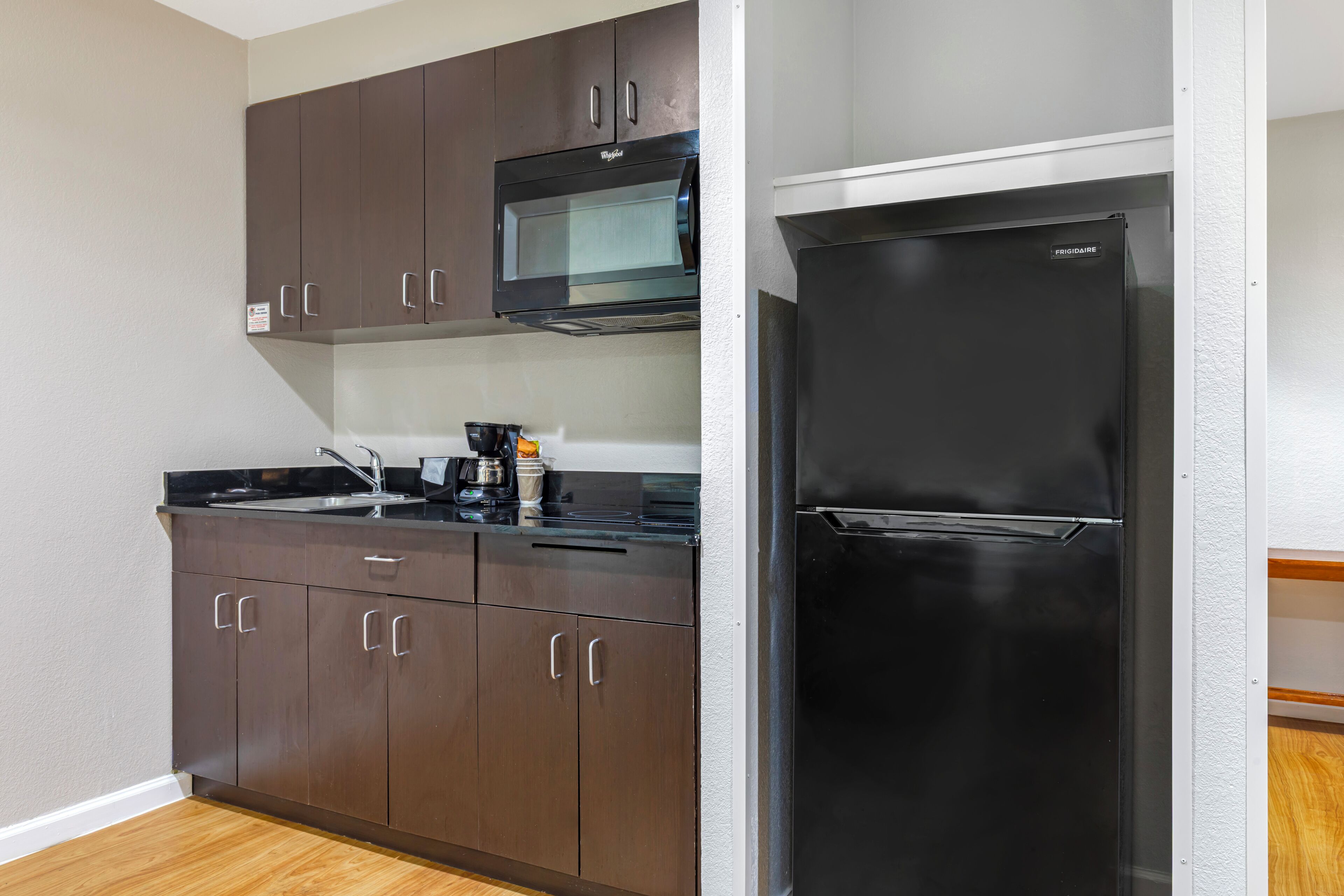 Una cocina compacta con armarios color café oscuro, un refrigerador negro y un microondas.