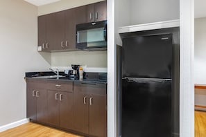 Una cocina compacta con armarios color café oscuro, un refrigerador negro y un microondas.