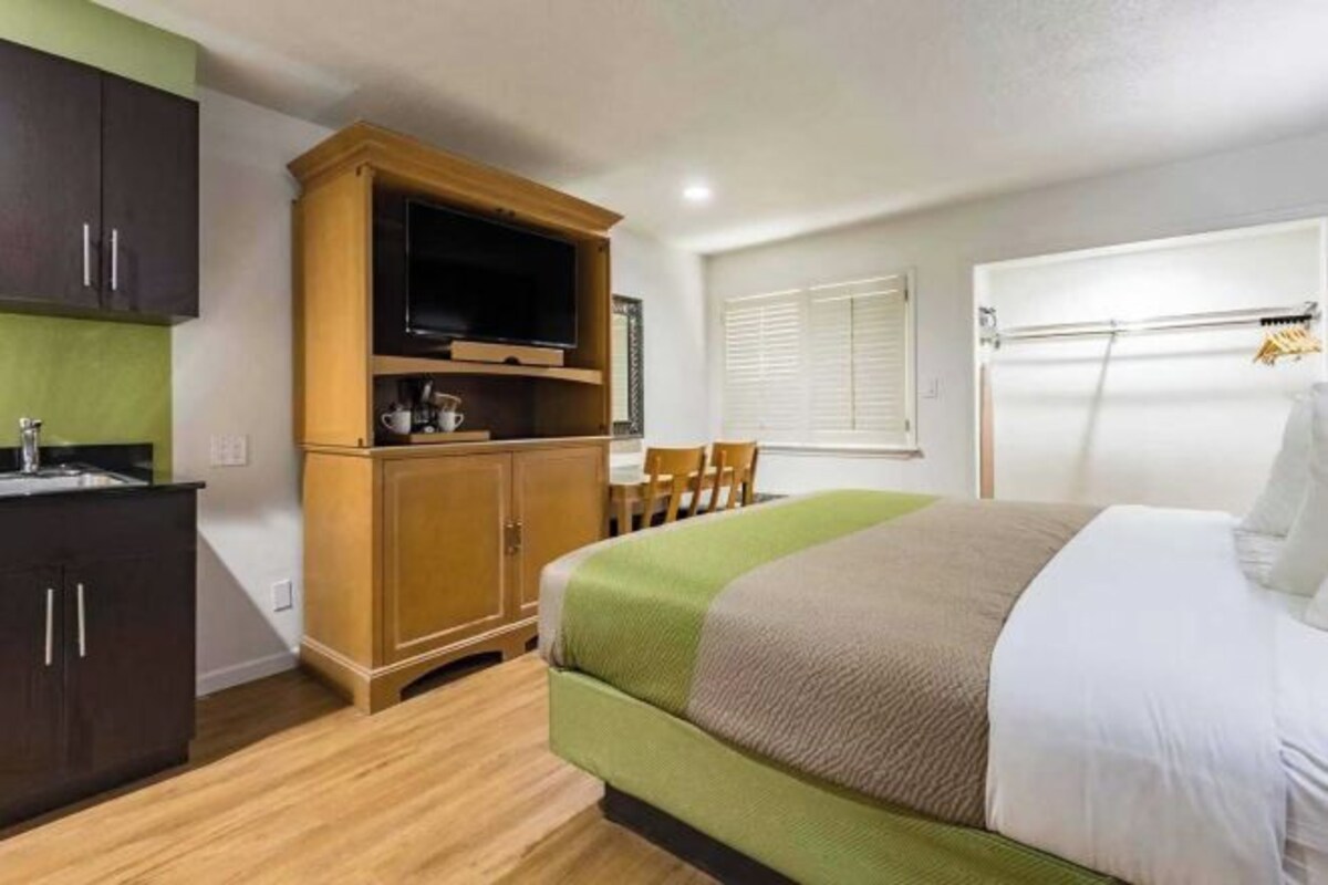A hotel room with a bed, a TV, a wooden cabinet, and a small table.