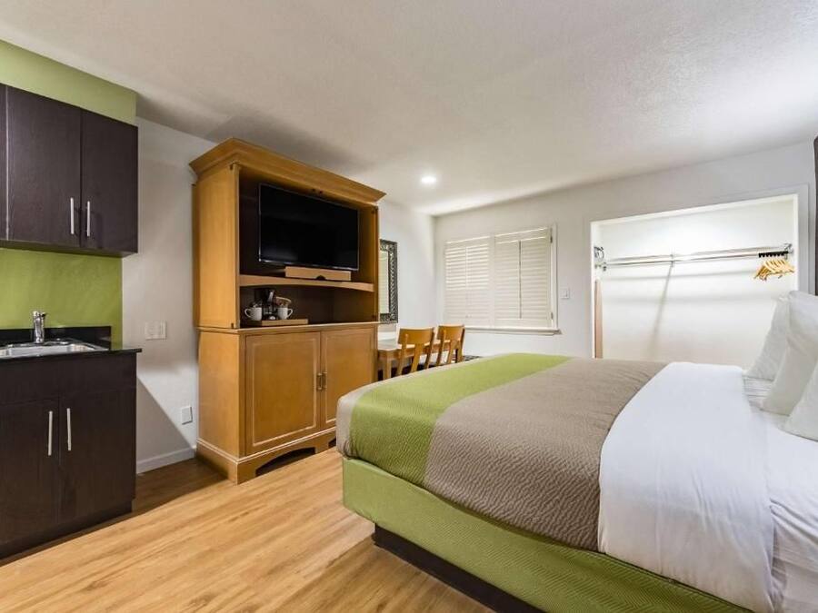 Una habitación de hotel compacta con cama, televisión, kitchenette y ventana con persianas.