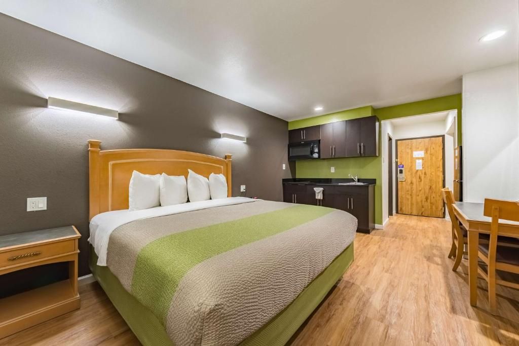 Ein Hotelzimmer mit Bett, Nachttisch, kleinem Schreibtisch, Stuhl, einer Küchenzeile und einer Tür.