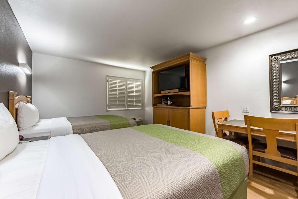 Una habitación de hotel con dos camas, un escritorio, un televisor y un espejo.