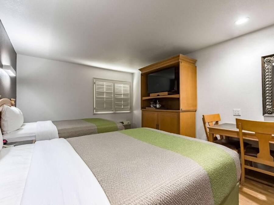 A hotel room with two beds, a desk, a television, and a mirror.