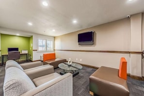 A hotel room with a sofa, armchair, ottoman, and a small coffee table. - Studio 6 Plano, TX (Plano)