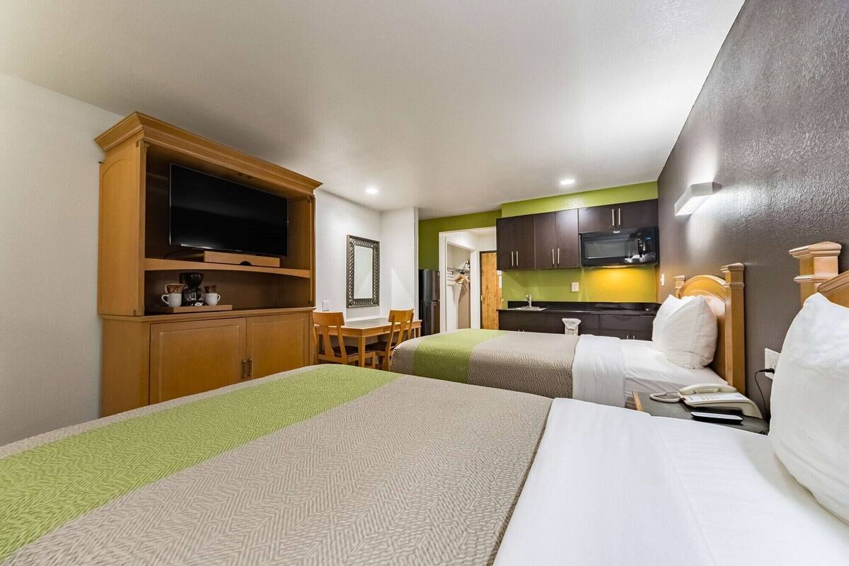 A hotel room with two beds, a TV, a mirror, a small kitchenette, and a dining area.