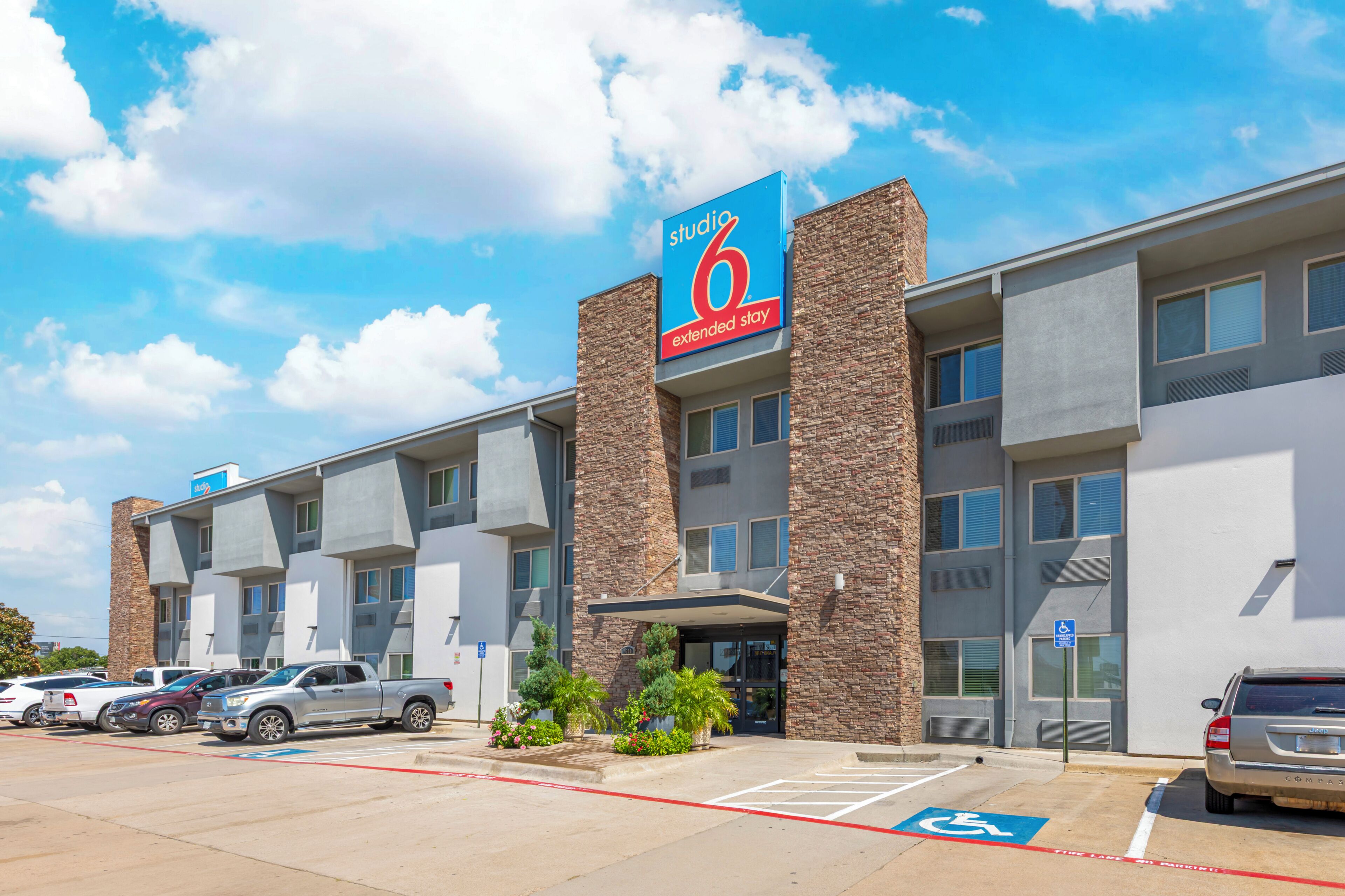 A 6 extended stay hotel with a modern design, parking lot, and a clear blue sky.