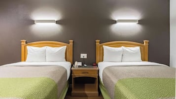 Habitación de hotel con dos camas, cada una con cabecero de madera y ropa de cama blanca. Entre las camas hay una mesita de noche con un teléfono y una lámpara pequeña.