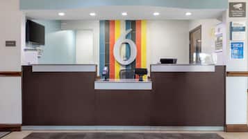 Un mostrador de recepción con un gran número '6' en la pared, una pantalla digital y una cámara de seguridad.