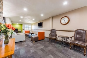 A lobby with seating, a clock, and a television. - Studio 6 Plano, TX (Plano)
