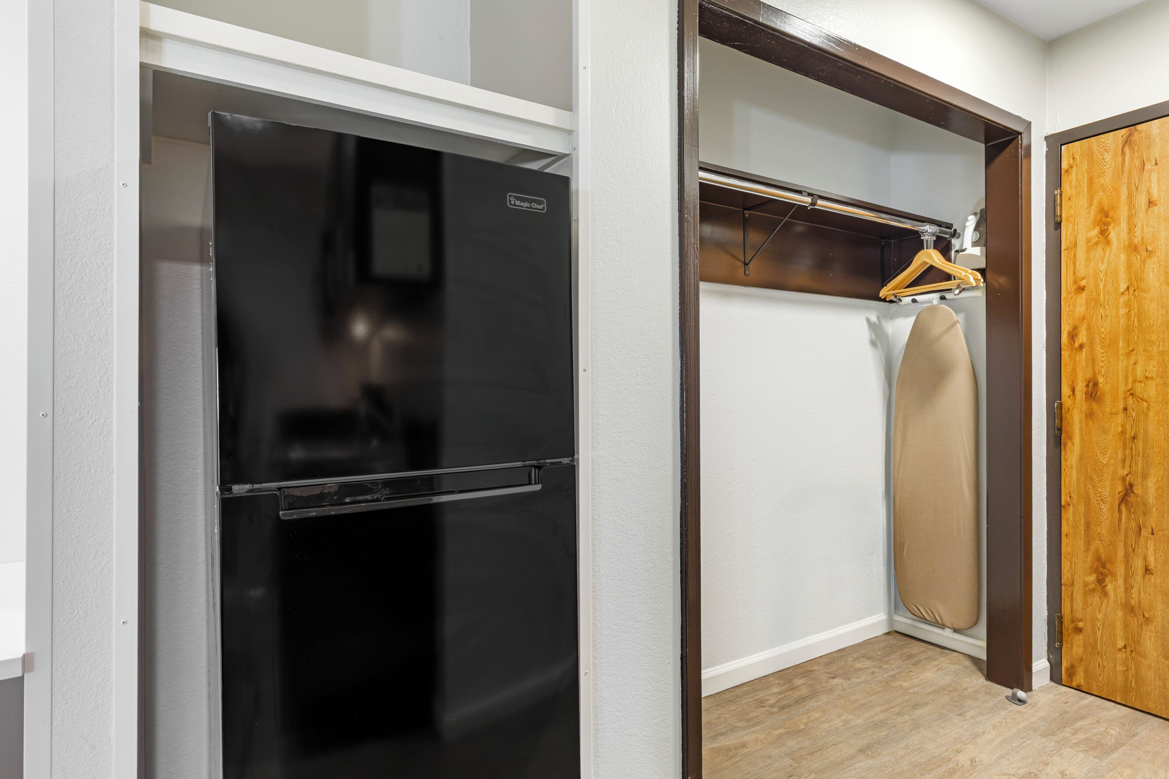 Cocina compacta con refrigerador negro, puerta de madera y un perchero.