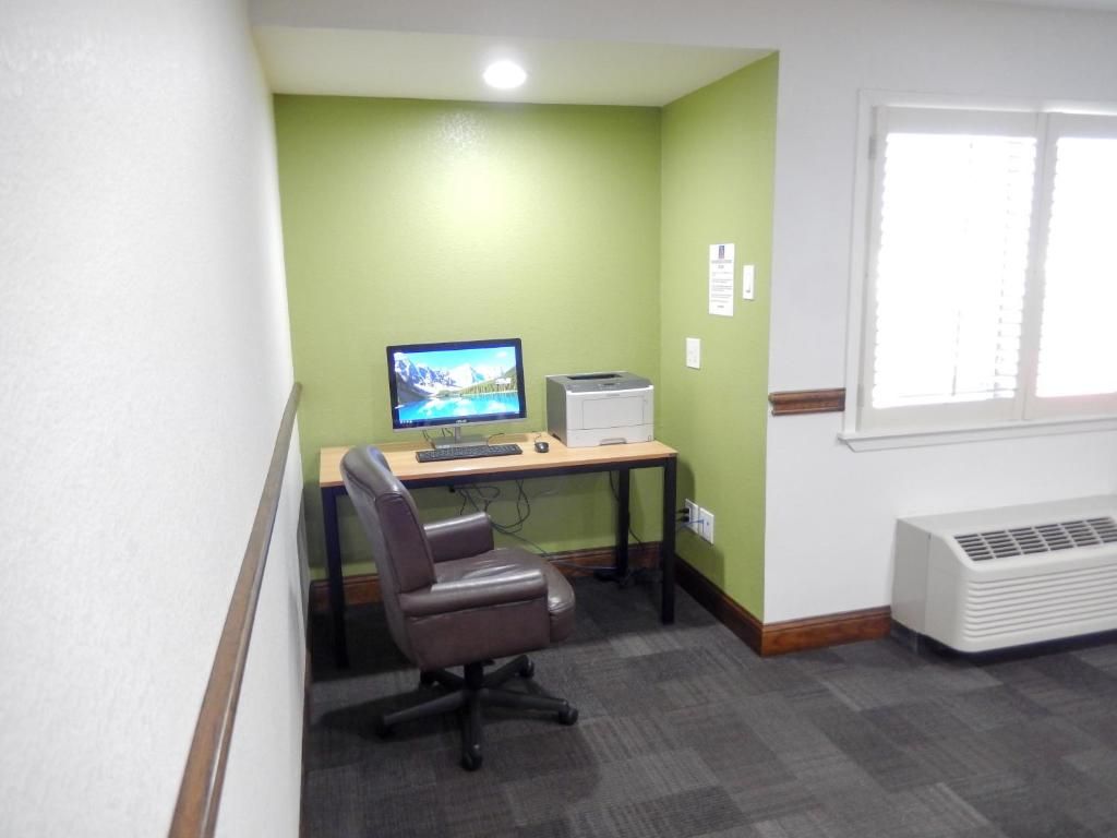 Un pequeño espacio de oficina con un escritorio, computadora, silla y una ventana con persianas.