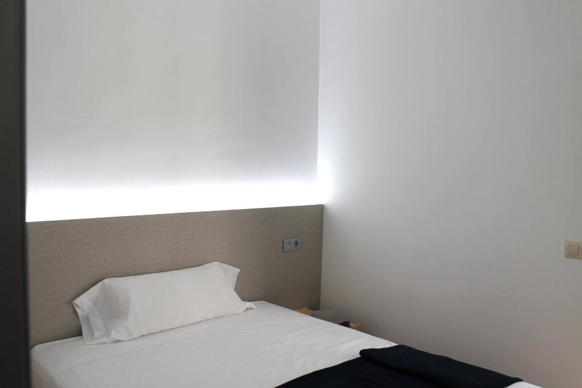 A small, single-bed room with a plain headboard, a white pillow, and a black blanket.