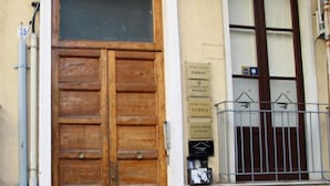 A wooden double door with a window above it, a metal balcony railing, and a sign on the wall indicating a library. - B&B del Toscano (Catania)