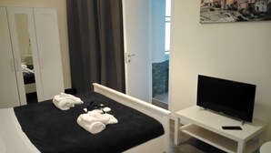 A hotel room with a bed, a TV on a stand, a wardrobe, and a painting on the wall. - B&B del Toscano (Catania)