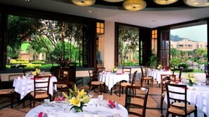 A restaurant with round tables set for dining, large windows offering a view of a landscaped garden, and a ceiling with circular light fixtures. - Cactus Resort Sanya by Gloria (Sanya)