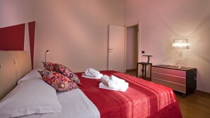 Ein ordentlich bezogenes Bett mit weißer und roter Bettwäsche, eine Nachttischlampe und eine Kommode mit einer Lampe.