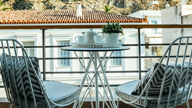 Un balcon avec deux chaises en métal et une petite table, donnant sur une colline sur laquelle se trouve un bâtiment.