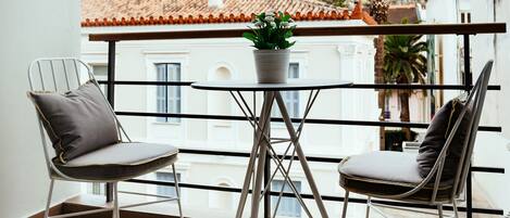Un balcon avec deux chaises et une petite table, donnant sur une colline rocheuse, avec des bâtiments visibles au loin.
