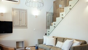 Un salon moderne avec un plancher en bois, un canapé gris, une chaise en bois, un escalier en verre et un téléviseur fixé au mur.
