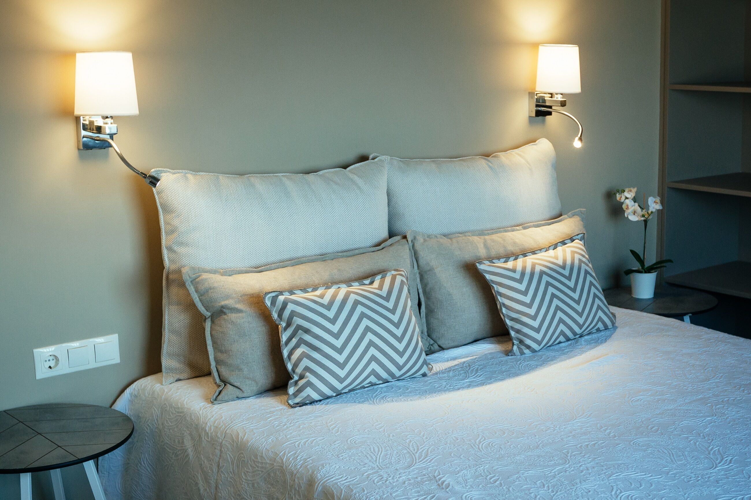 A neatly made bed with two pillows, a small round table, and two wall-mounted lamps.