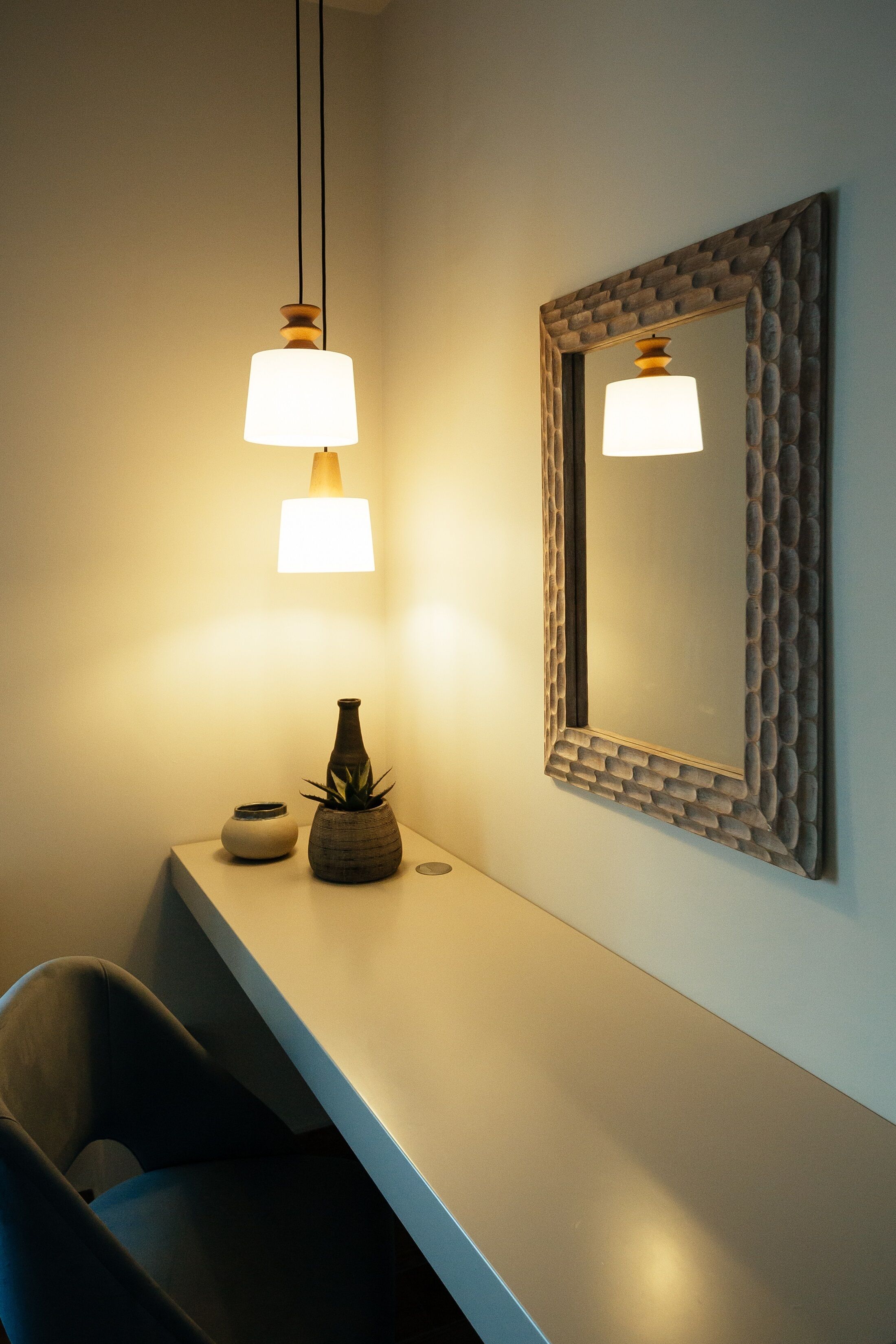 A modern bathroom with a white vanity, a mirror with a textured frame, and two pendant lights.