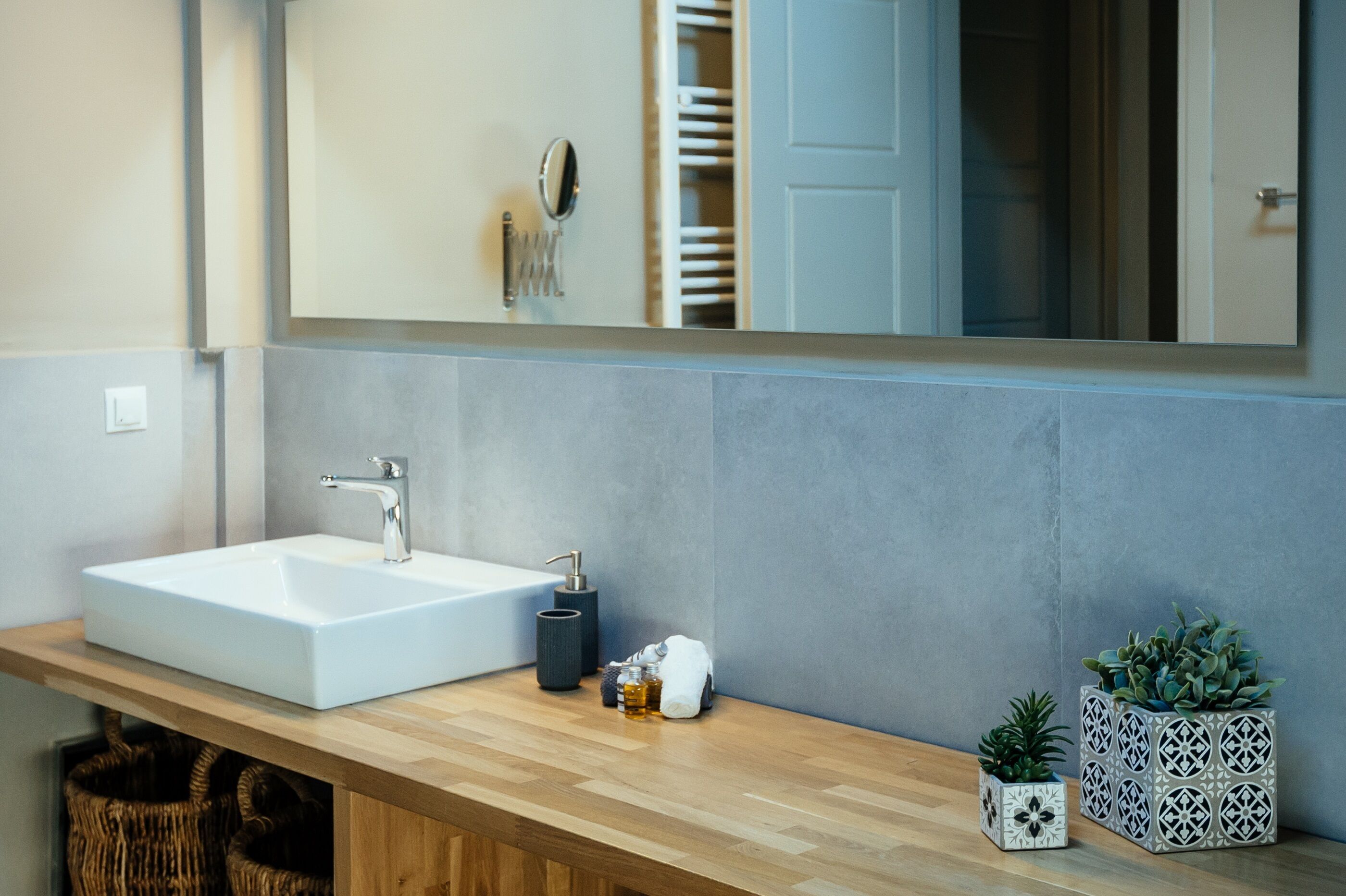 A modern bathroom with a large mirror, a white sink, and two potted plants.